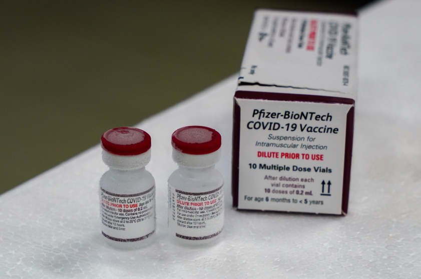 Dois frascos da vacina Pfizer-BioNTech contra a COVID-19, voltada para crianças de 6 meses a menores de 5 anos, estão congelados ao lado de uma embalagem com instruções de uso. A caixa destaca em letras vermelhas a necessidade de diluição antes da aplicação intramuscular.