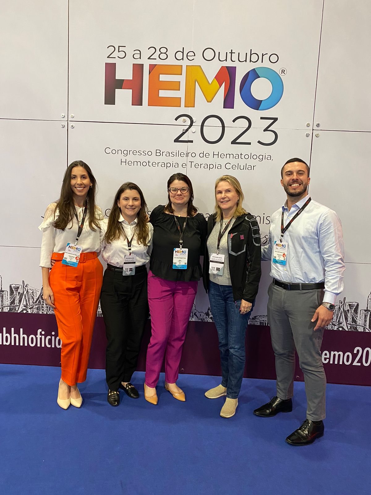 Cinco profissionais posando para foto em frente ao painel do Congresso Brasileiro de Hematologia, Hemoterapia e Terapia Celular HEMO 2023.