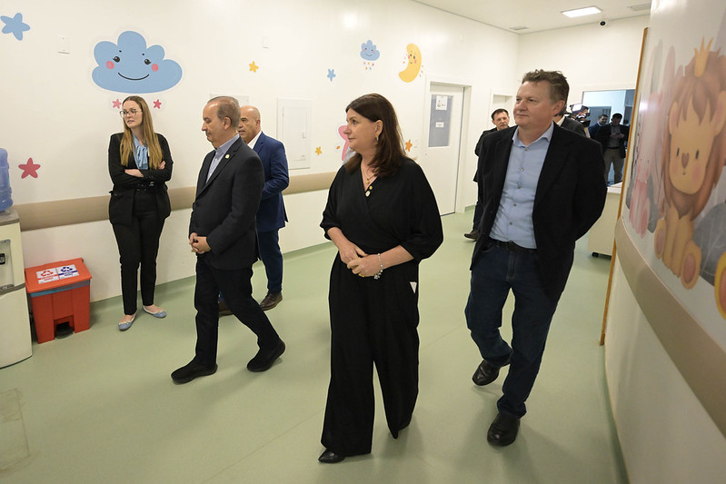 Autoridades caminham por corredor decorado com desenhos infantis em hospital pediátrico, observando a estrutura recém-reformada do Hospital Materno-Infantil Santa Catarina.