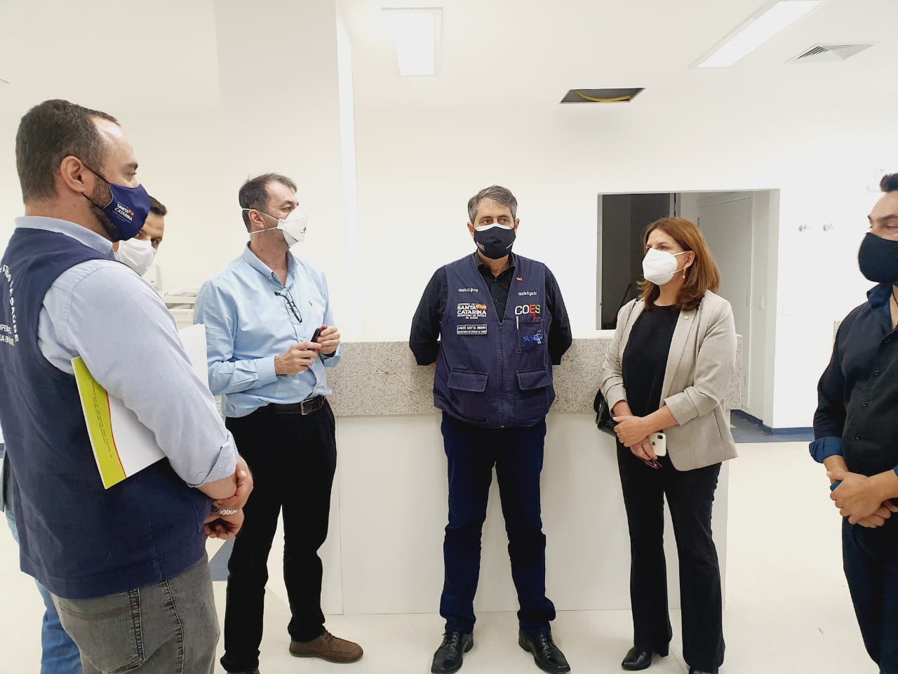 Secretário de Saúde de Santa Catarina e cinco profissionais reunidos em pé no interior do Hospital Tereza Ramos em Lages, durante anúncio da retomada das obras e ampliação de leitos de UTI.
