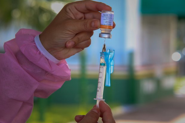 Mão de profissional da saúde carregando seringa com frasco de vidro