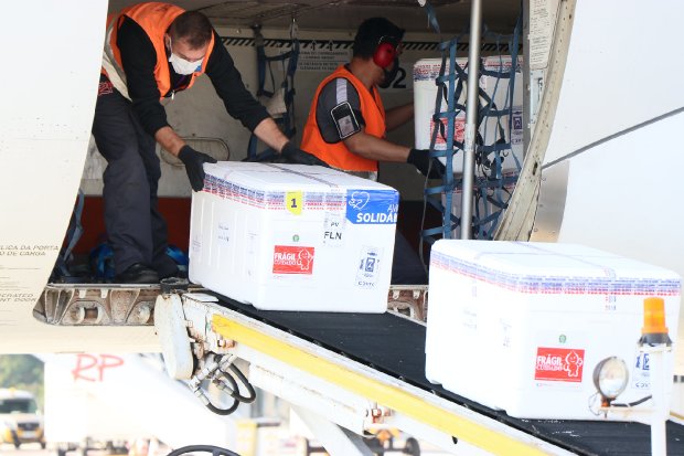 Dois homens de cabelo curto colocando caixas térmicas em esteiras para retira-las do avião.