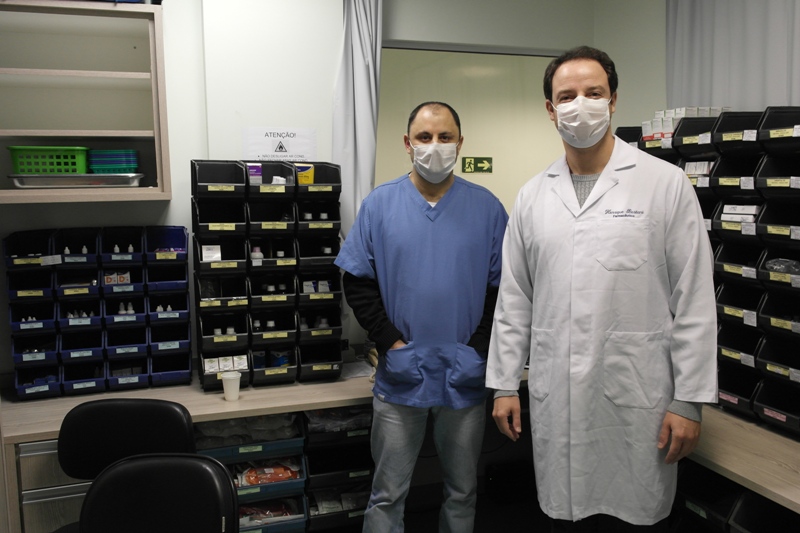 Dois profissionais da saúde posam para foto dentro de sala 