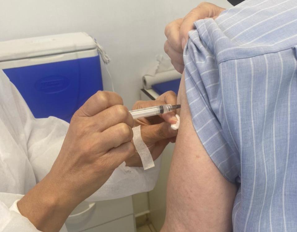 Profissional de saúde aplicando vacina contra COVID-19 no braço de pessoa vestindo camisa listrada azul e branca, representando a campanha de vacinação de Santa Catarina - um dos 10 estados que mais vacinaram no país.