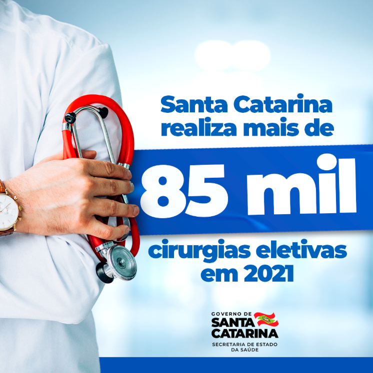 Card informativo com fundo azul e imagem parcial de um profissional da saúde segurando um estetoscópio vermelho. O texto diz: 'Santa Catarina realiza mais de 85 mil cirurgias eletivas em 2021'. No canto inferior direito, está o logotipo do Governo de Santa Catarina com a inscrição 'Secretaria de Estado da Saúde'.